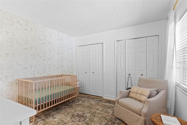 bedroom featuring a nursery area, multiple closets, a textured ceiling, and wallpapered walls