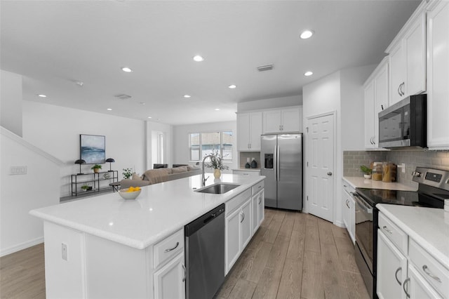 kitchen with visible vents, an island with sink, light wood-style flooring, appliances with stainless steel finishes, and a sink