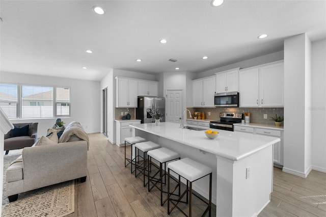 kitchen with stainless steel appliances, a sink, light wood-style flooring, and a kitchen breakfast bar