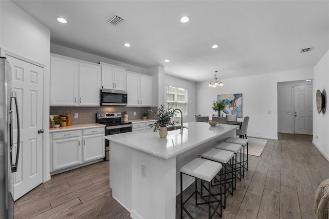 kitchen with stainless steel appliances, wood finished floors, visible vents, and white cabinets