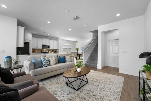 living area featuring recessed lighting, wood finished floors, visible vents, and stairs