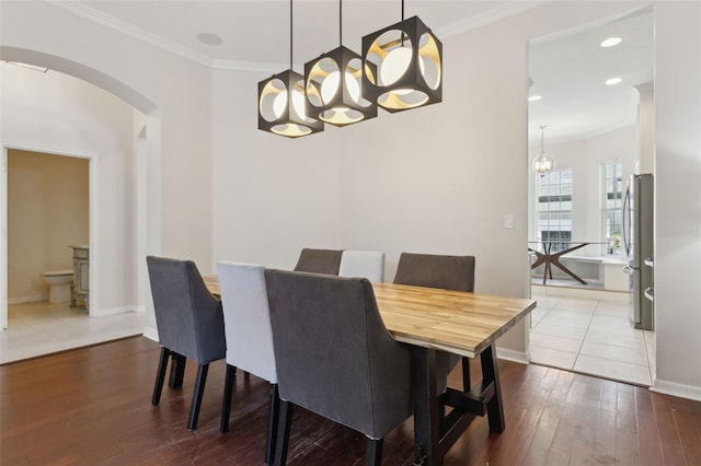 dining area with baseboards, ornamental molding, arched walkways, and hardwood / wood-style floors