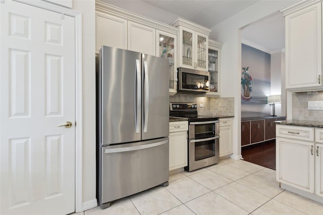 kitchen with light tile patterned floors, dark stone counters, glass insert cabinets, stainless steel appliances, and backsplash