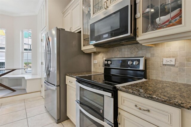 kitchen with light tile patterned floors, tasteful backsplash, glass insert cabinets, ornamental molding, and stainless steel appliances