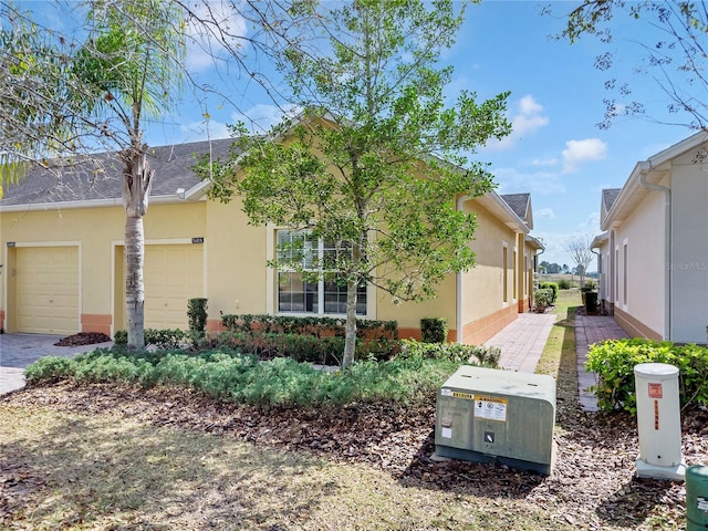 view of side of property featuring decorative driveway, an attached garage, and stucco siding