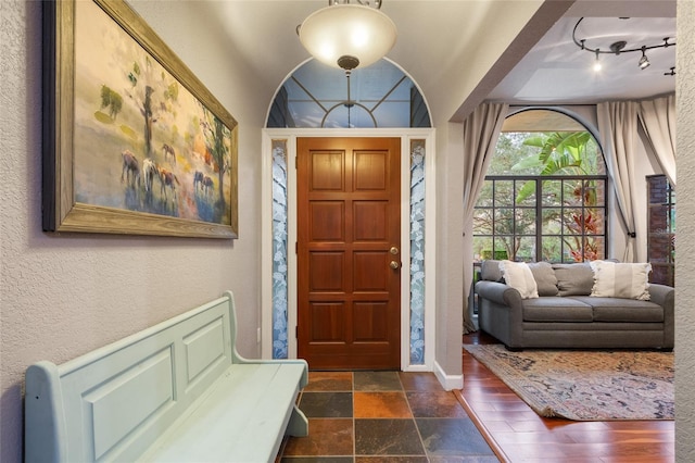 entryway featuring track lighting, stone tile flooring, a textured wall, and baseboards