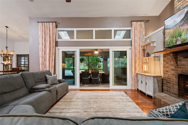 living room with plenty of natural light, a brick fireplace, wood finished floors, and a notable chandelier