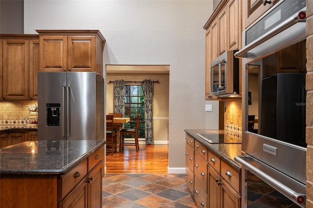 kitchen featuring appliances with stainless steel finishes, brown cabinetry, backsplash, and baseboards