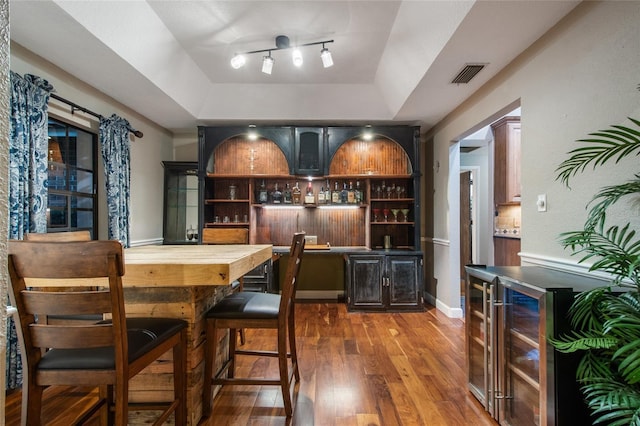 bar with a tray ceiling, indoor wet bar, visible vents, wood finished floors, and beverage cooler