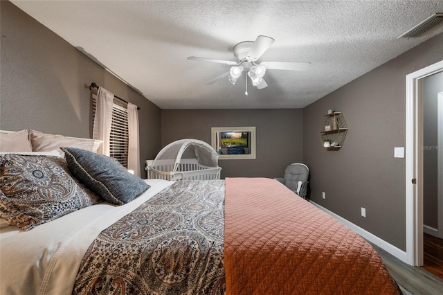 bedroom with a textured ceiling, ceiling fan, wood finished floors, visible vents, and baseboards