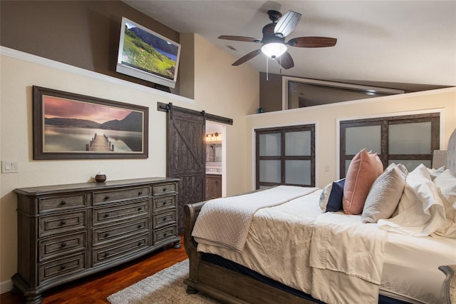 bedroom with a barn door, connected bathroom, ceiling fan, dark wood-style flooring, and vaulted ceiling