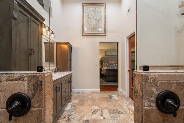 bathroom featuring vanity, a towering ceiling, stone tile flooring, and baseboards