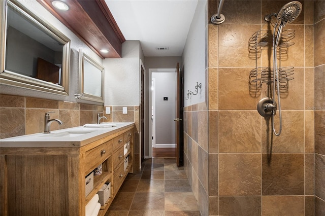 full bathroom featuring double vanity, visible vents, tile walls, a tile shower, and a sink