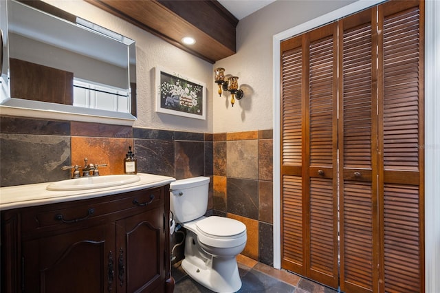 bathroom with toilet, vanity, tile walls, a closet, and stone finish flooring