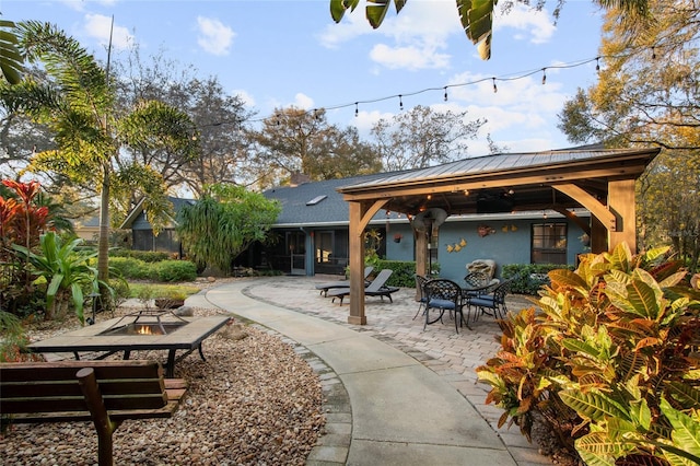 back of house with metal roof, an outdoor fire pit, a patio, a gazebo, and stucco siding