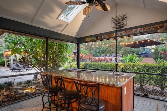 sunroom featuring lofted ceiling with skylight, bar area, a sink, and ceiling fan