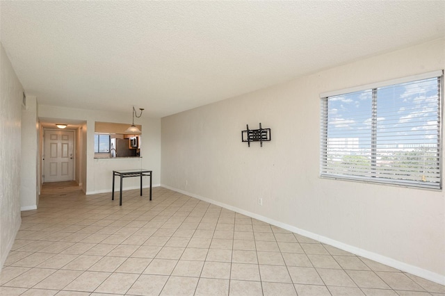 spare room featuring light tile patterned floors, baseboards, and a textured ceiling