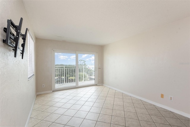 spare room featuring a textured ceiling, light tile patterned flooring, and baseboards