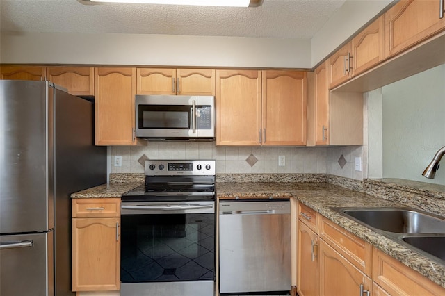 kitchen with a textured ceiling, decorative backsplash, stainless steel appliances, and a sink