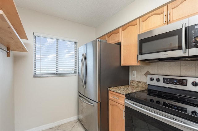 kitchen featuring light tile patterned floors, a textured ceiling, baseboards, appliances with stainless steel finishes, and tasteful backsplash