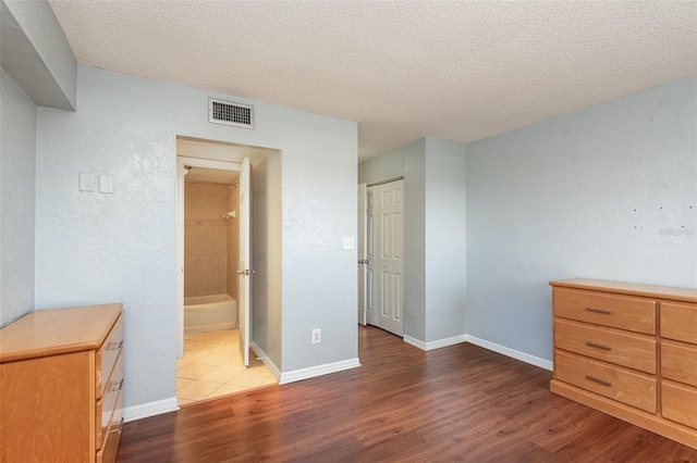 bedroom featuring baseboards, visible vents, wood finished floors, ensuite bathroom, and a textured ceiling