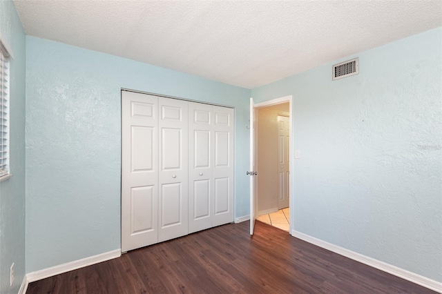 unfurnished bedroom featuring baseboards, a closet, visible vents, and wood finished floors