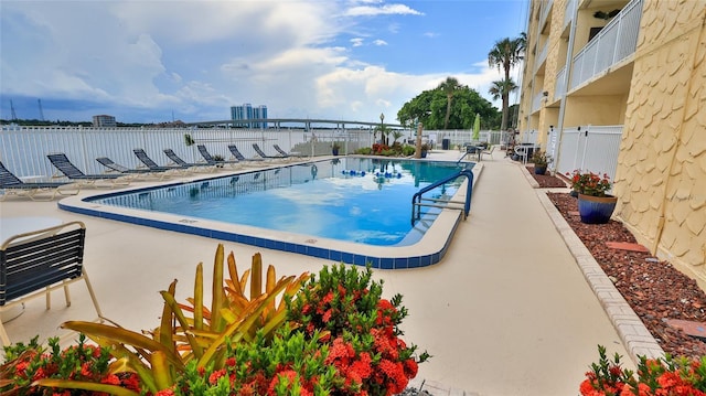 community pool with a patio area, fence, and a city view