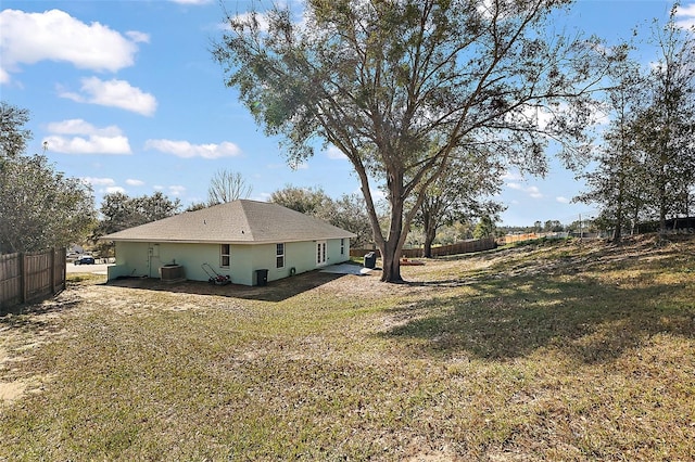 view of side of property with central air condition unit, fence, a lawn, and stucco siding