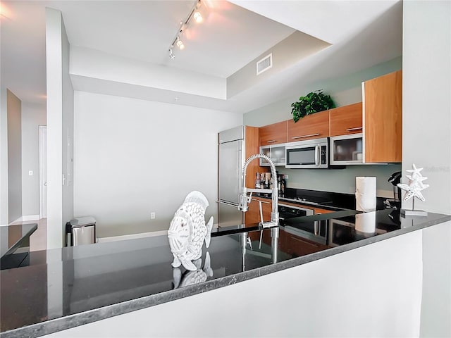 kitchen featuring brown cabinets, stainless steel microwave, visible vents, and built in fridge