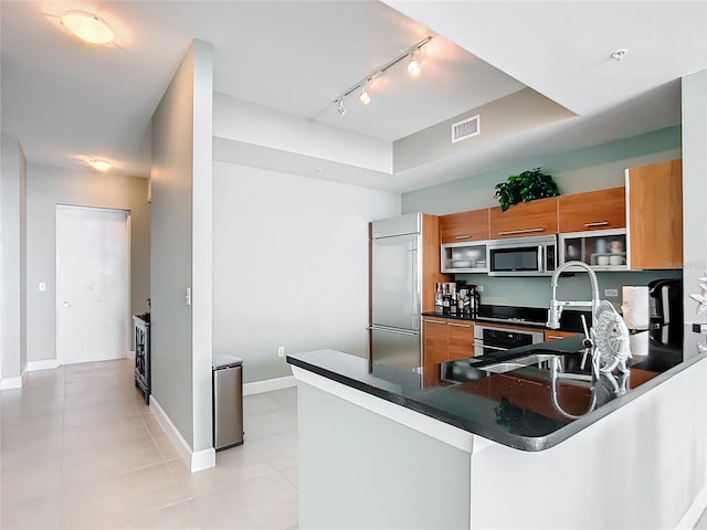 kitchen featuring visible vents, brown cabinetry, dark countertops, a peninsula, and stainless steel appliances