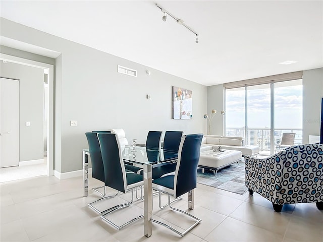 dining space featuring rail lighting, visible vents, light tile patterned flooring, a wall of windows, and baseboards