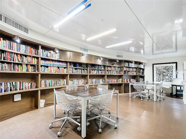 office area featuring visible vents, concrete floors, and wall of books