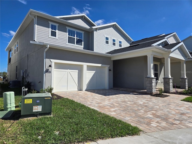 craftsman-style home with an attached garage, decorative driveway, and stucco siding