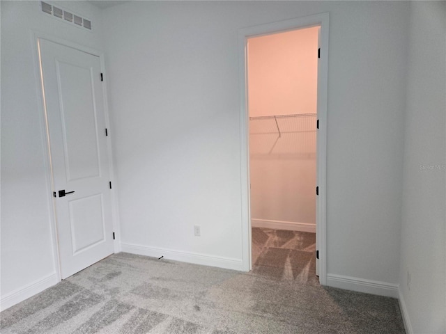 unfurnished bedroom featuring a spacious closet, carpet flooring, visible vents, and baseboards