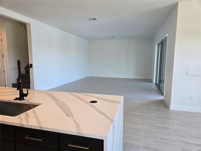 kitchen with dark cabinetry, a sink, visible vents, and light stone countertops