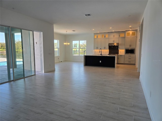 unfurnished living room featuring an inviting chandelier, baseboards, visible vents, and a sink