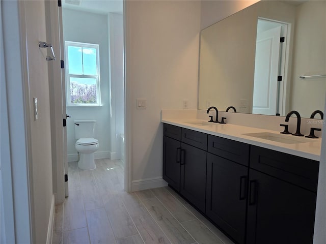 bathroom with toilet, double vanity, baseboards, and a sink