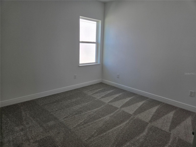 unfurnished room featuring dark carpet and baseboards