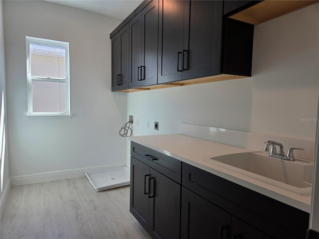 interior space featuring light wood-style floors, light countertops, a sink, and baseboards