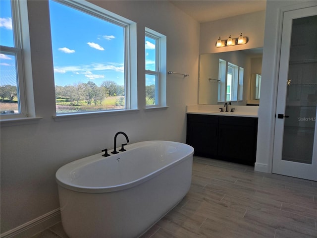 full bathroom with wood finish floors, a soaking tub, vanity, and baseboards