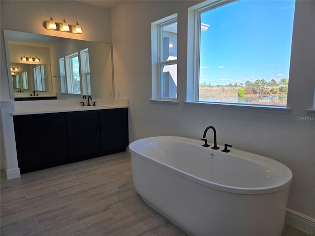 bathroom with a soaking tub, vanity, a wealth of natural light, and wood finish floors