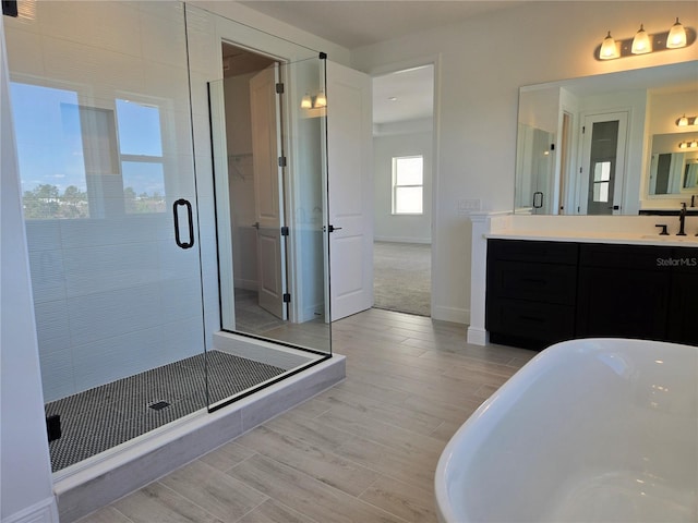 bathroom with wood finish floors, a stall shower, a soaking tub, and vanity