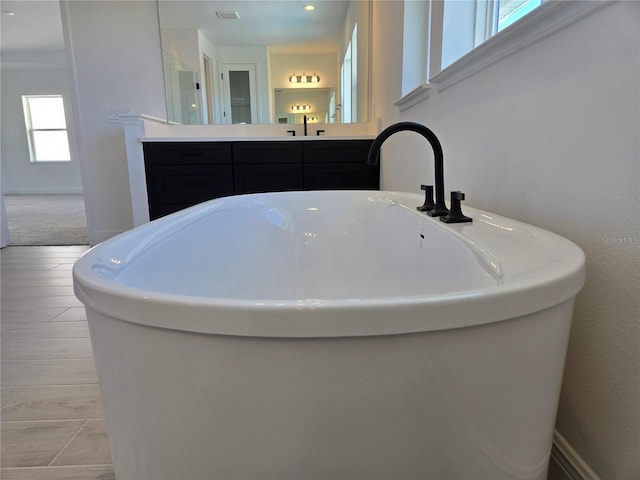 bathroom featuring a freestanding tub, visible vents, baseboards, and vanity