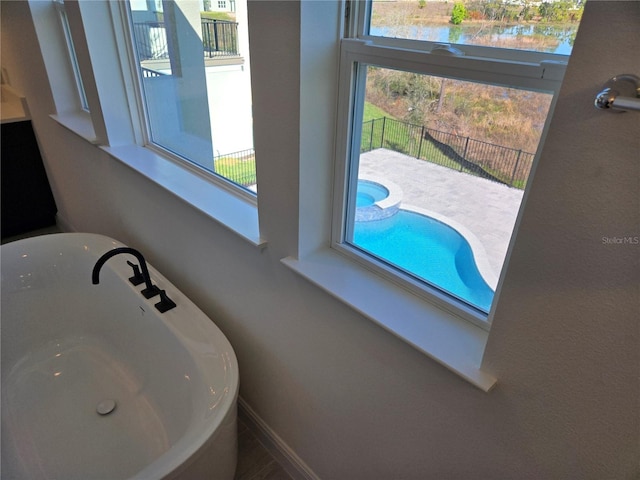 room details featuring a water view, a freestanding bath, baseboards, and a sink