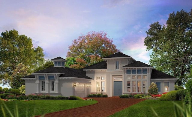 prairie-style home featuring an attached garage, stucco siding, decorative driveway, and a yard