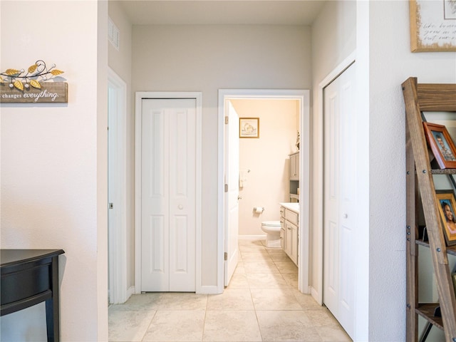 hallway with light tile patterned floors, visible vents, and baseboards