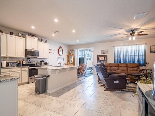 kitchen with open floor plan, appliances with stainless steel finishes, visible vents, and light stone countertops