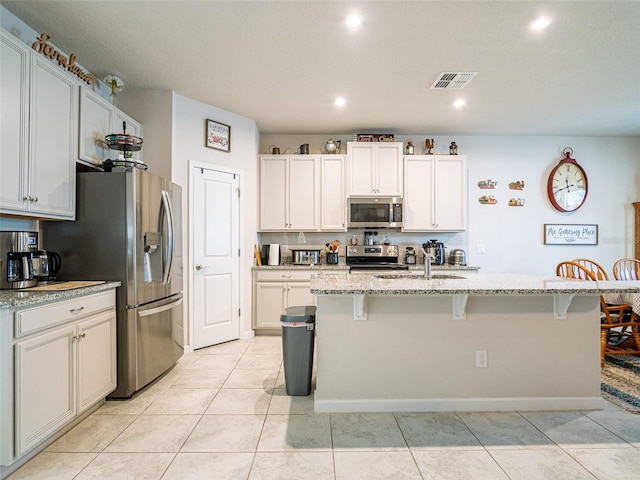 kitchen with light stone counters, a breakfast bar area, stainless steel appliances, a sink, and visible vents