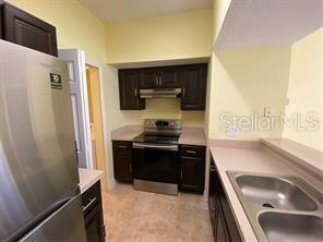 kitchen with under cabinet range hood, a sink, light countertops, appliances with stainless steel finishes, and dark brown cabinets