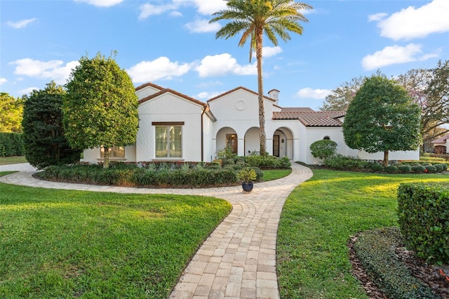 mediterranean / spanish home with a tile roof, a front lawn, and stucco siding